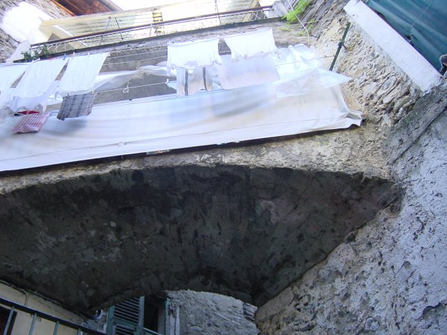 An arch between two building transformed as a corridor with laundry drying. Isolabona, Italy