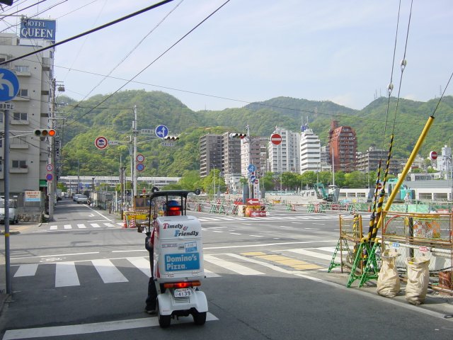 En descendant de la gare vers le centre ville, une vegetation dense sur les collines, et l'invasion des pseudo-pizzas au premier plan. Kobe, Japon.